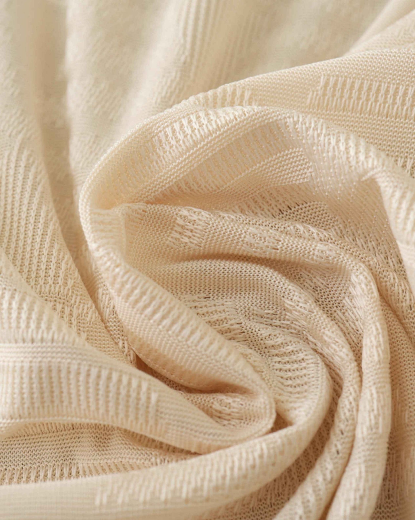 A close-up of a cream-colored knitted fabric with a textured pattern.