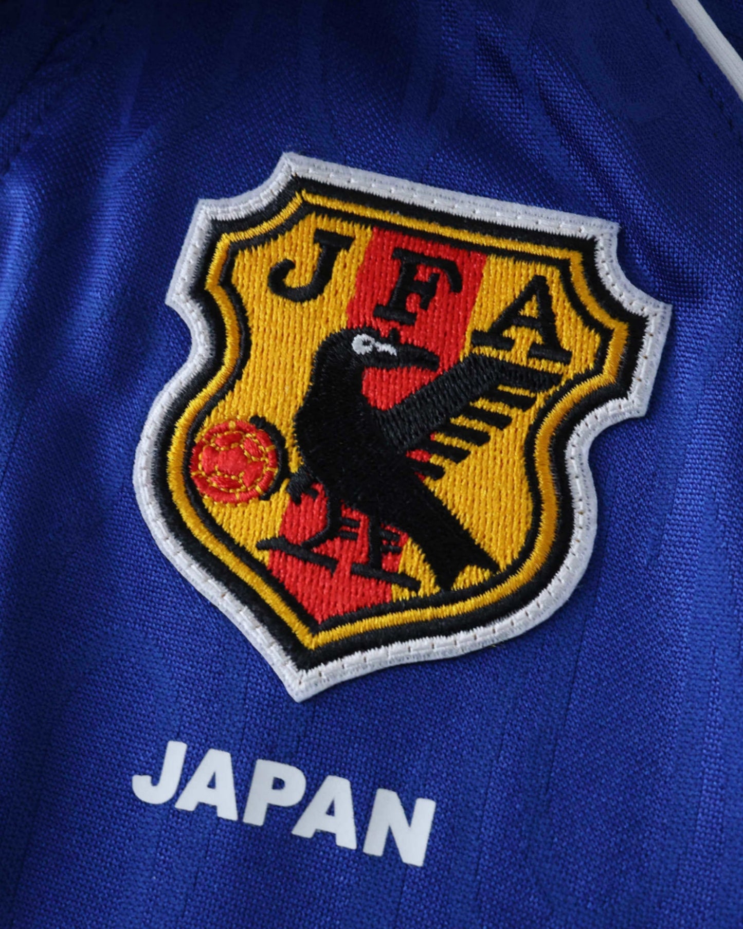 Close-up of JFA crow crest and JAPAN text on the blue 1998 retro kids football jersey