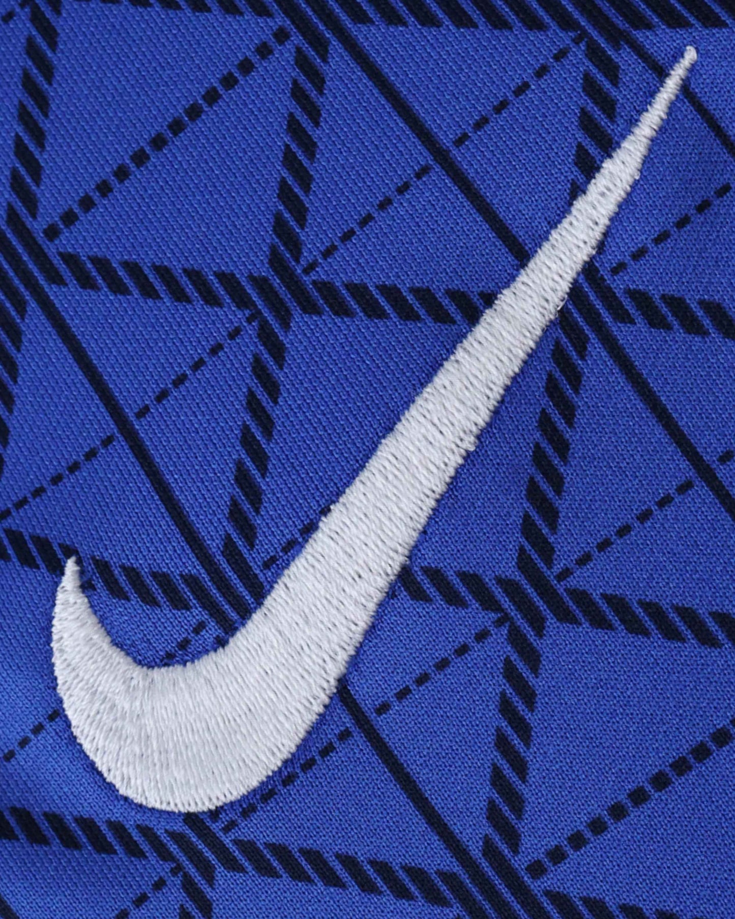 A white Nike swoosh logo is embroidered on a blue fabric with a black geometric pattern.