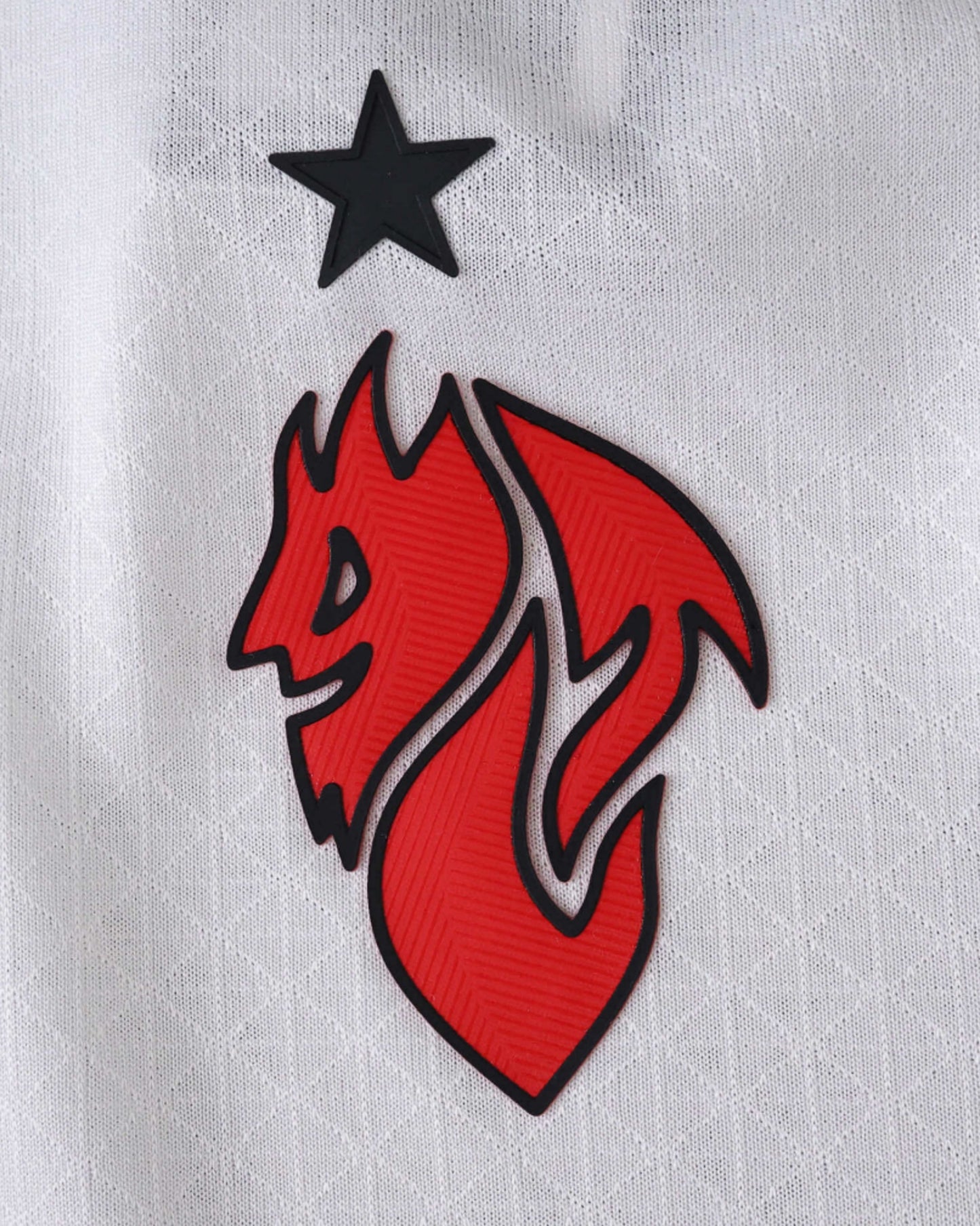 Close-up of a red and black devil logo with a black star on a white textured AC Milan jersey.