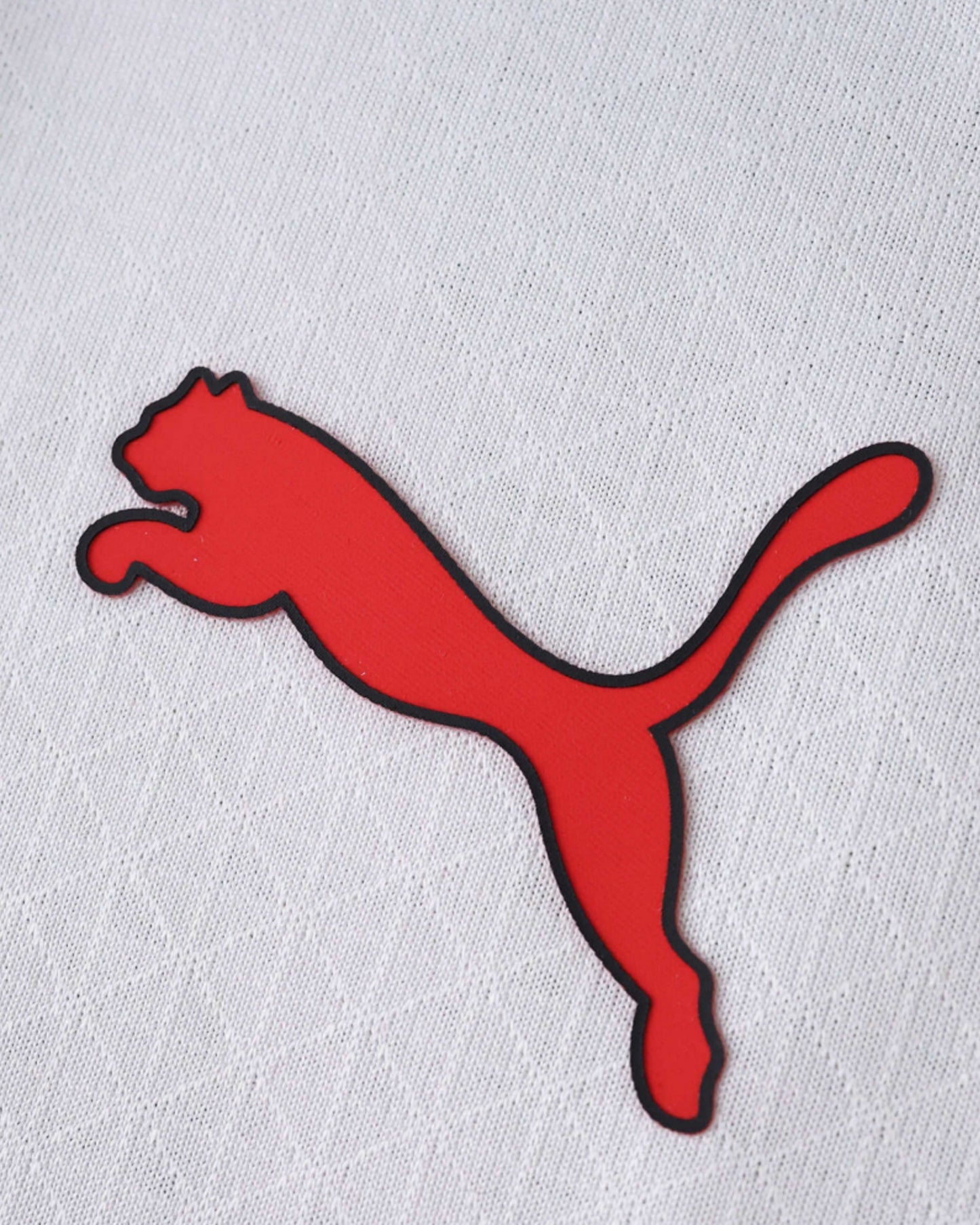 Close-up of a red and black Puma logo on a white textured AC Milan away jersey.