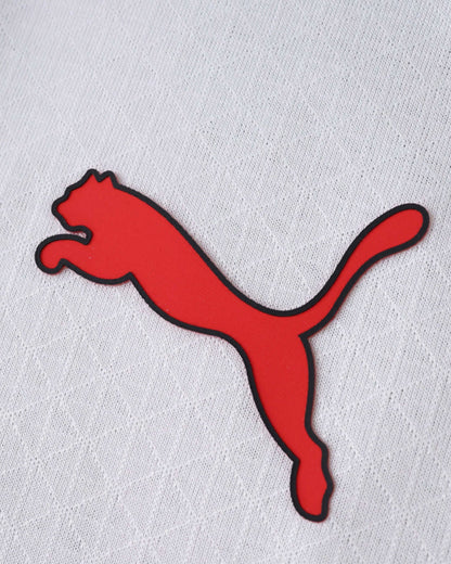 Close-up of a red and black Puma logo on a white textured AC Milan away jersey.