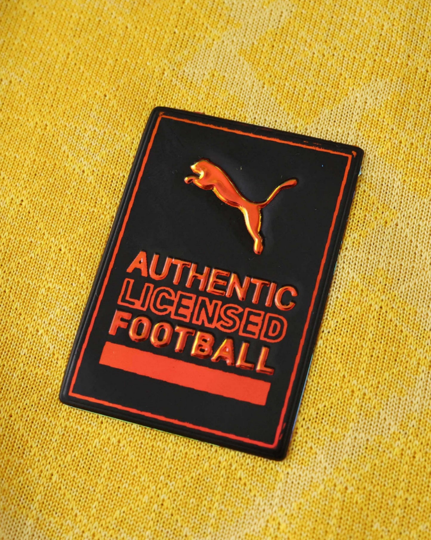 A black and orange Puma badge on a yellow textured fabric.