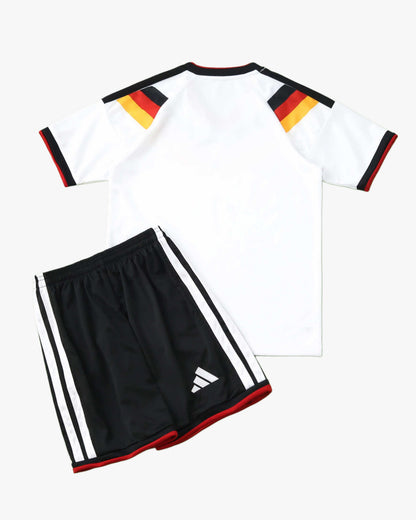 A white Germany home soccer jersey with black, red, and gold shoulder stripes and black shorts.
