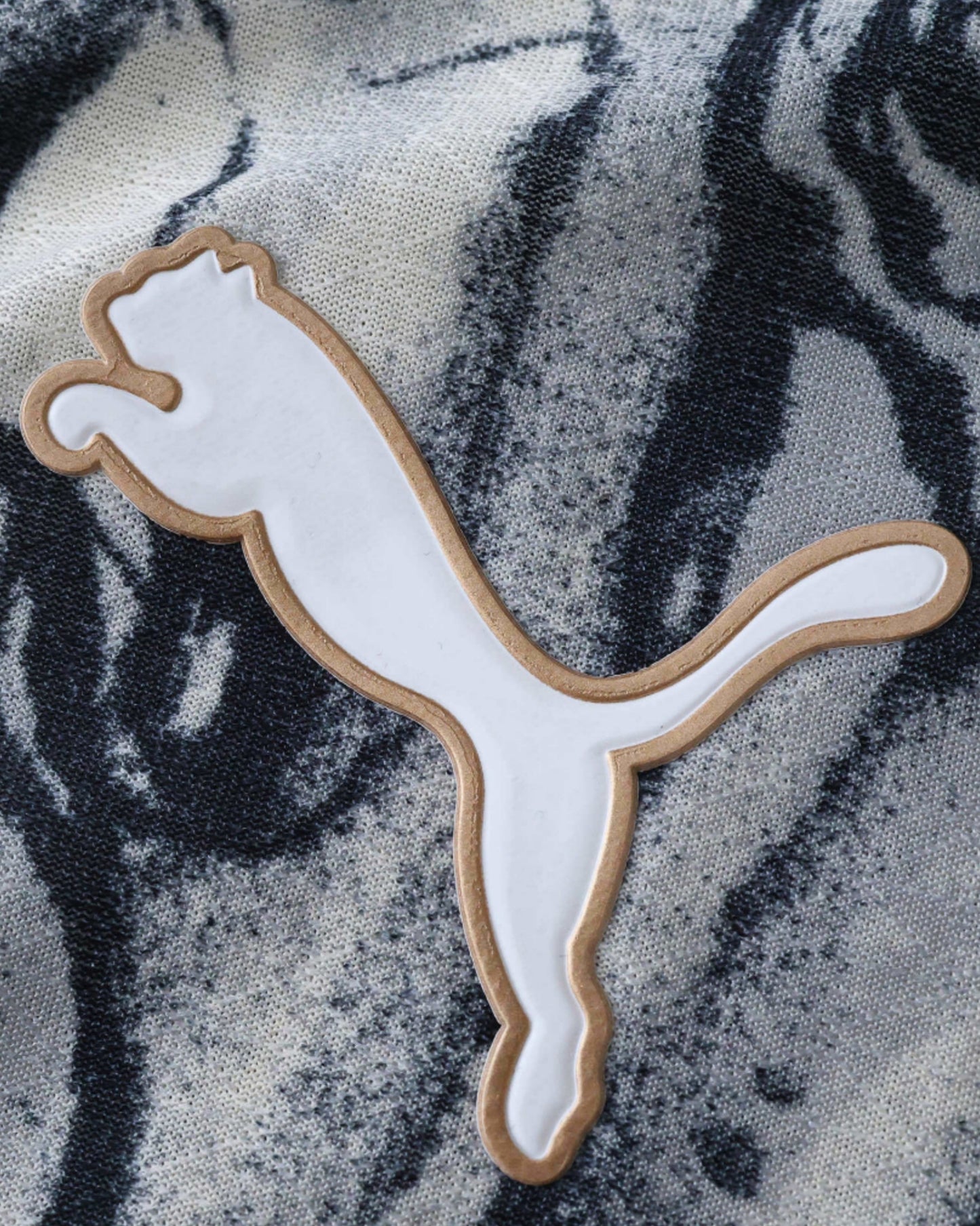 A white Puma logo with a gold outline on a black and white patterned fabric.