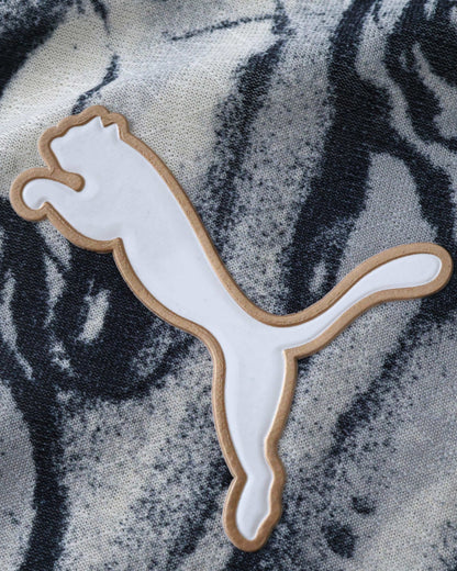 A white Puma logo with a gold outline on a black and white patterned fabric.