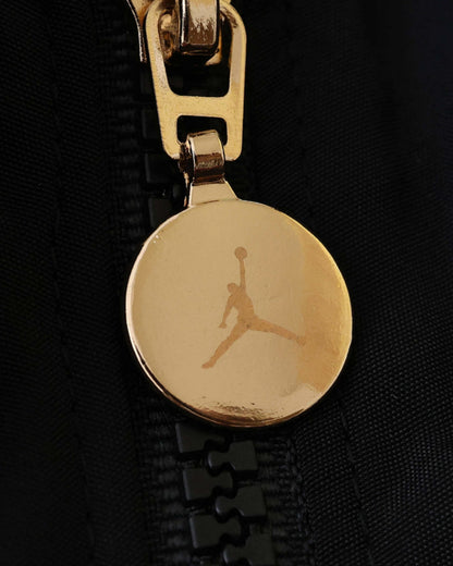 Gold Jordan Jumpman logo on a black zipper pull of a jacket.